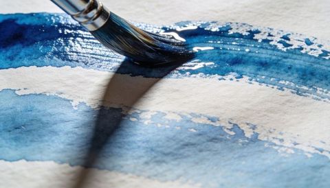 Applying Round Watercolor Brush Creating Wet Indigo Blue Stroke on Textured Paper Closeup