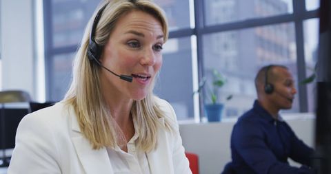 Professional woman and colleague in office wearing headsets engaged in conversation with clients. Useful for illustrating modern customer service, communication, teamwork, and office professionalism. Perfect for corporate presentations, websites, and marketing materials highlighting business environments.