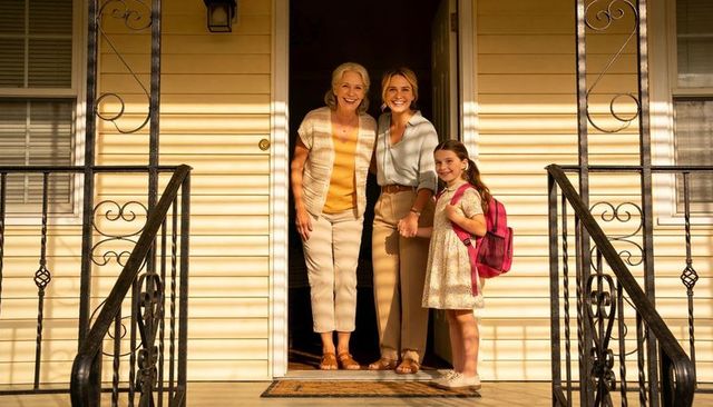 Smiling three-generation family welcoming on sunlit porch holding hands with pink backpack
