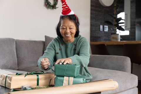 Asian woman in festive attire wrapping holiday gifts at home