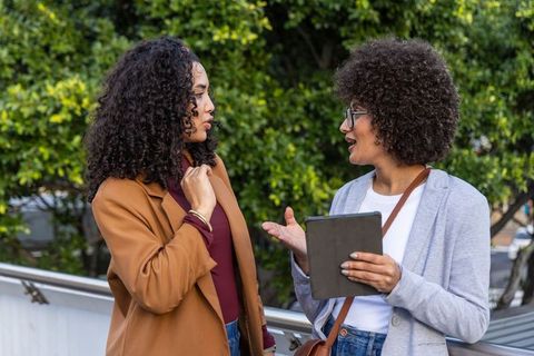 African-american women collaborating on tablet on balcony, casual business conversation