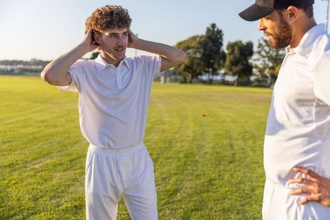 Young teammate discussing tactics with coach on sunlit green field training session