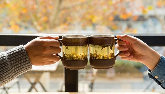 Clinking glass mugs of loose tea by window, cozy sweaters, autumn morning