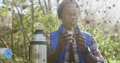 Sipping warm drink in wilderness while camping: man wearing blue vest holding metal cup