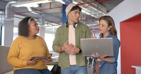Multicultural team collaborating in modern open office lounge with laptop and tablet