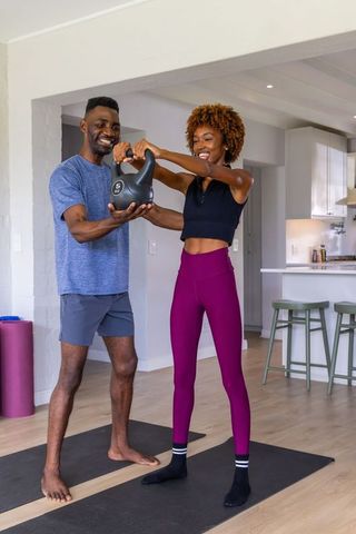 Diverse couple training with 5kg kettlebell in bright home kitchen workout session