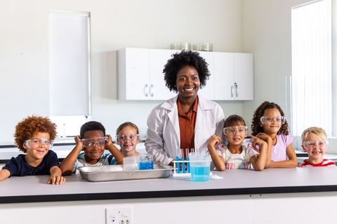 African american teacher leading elementary science lab with diverse students in safety goggles