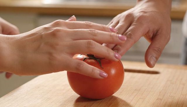 Close-up two hands steadying ripe tomato on wooden cutting board for home cooking