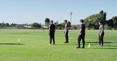 Coach leading male players through cone drill on sunny grass field for team training