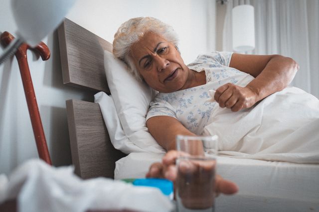 African american senior woman reaching out for glass of water while lying in the bed at home. retirement senior lifestyle living in quarantine lockdown concept
