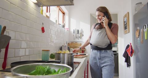 Caucasian mother multitasking with baby carrier in kitchen