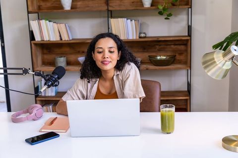 African american woman recording podcast from home office with laptop and microphone
