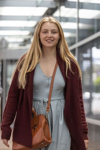 Young woman walking through transit concourse wearing dress, cardigan, leather crossbody bag