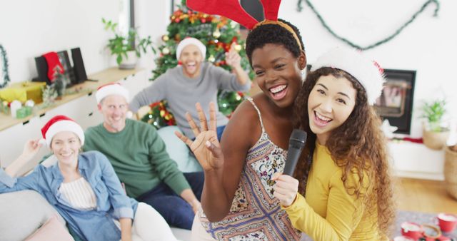 Friends are celebrating Christmas by singing karaoke at a festive home party. Christmas tree and holiday decorations add to the joyful atmosphere. This image is perfect for promoting holiday events, social gatherings, party invitations, and festive season activities. Ideal for use in advertisements, holiday cards, and festive season social media posts.