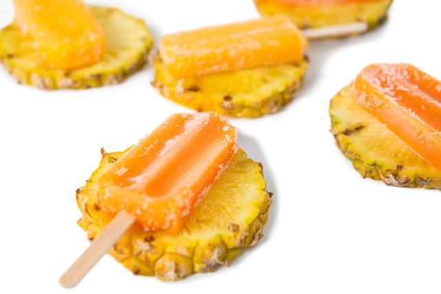 Refreshing orange popsicles placed on pineapple slices, perfect for summer treats and tropical-themed parties. Ideal for use in food blogs, summer recipe collections, and advertisements for frozen desserts.