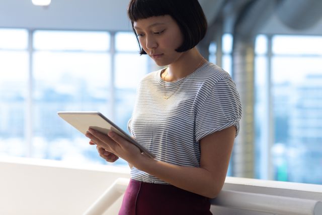 Young businesswoman using a digital tablet in a modern office environment. Ideal for themes related to technology in the workplace, professional women, modern business practices, and corporate settings. Useful for articles, blogs, and marketing materials focusing on business, technology, and professional development.