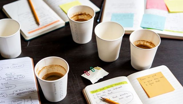 Caffeine-fueled brainstorming with paper coffee cups, open notebooks and sticky notes