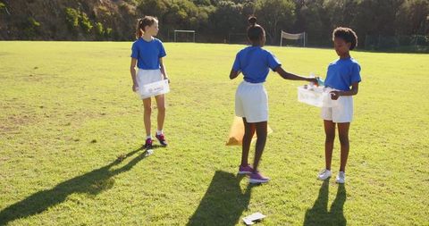 Young Girls Collecting Bottles on Sunny Field for Team Collaboration