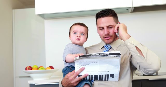 Father carrying his baby son before work and talking on phone at home in the kitchen