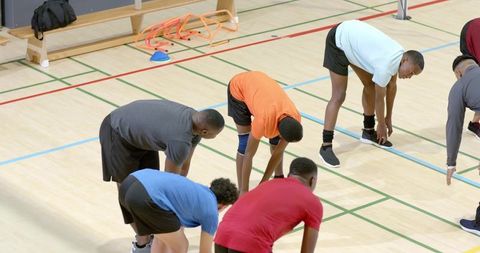 Diverse male athletes stretching together in gymnasium during team warmup and agility drills