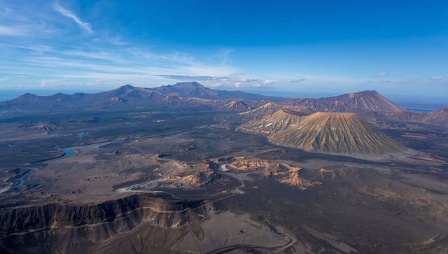 Aerial panorama showcasing volcanic cone rising from layered lava plain with winding track