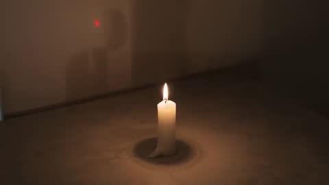 Candle flickering on table with melting wax ring and red laser dot casting silhouette