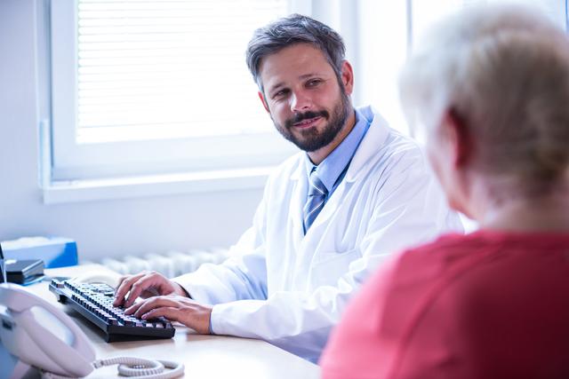 Doctor in white coat interacting with patient while working on computer in medical office. Ideal for use in healthcare, medical consultation, doctor-patient relationship, and hospital-related content.