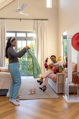 Friends choosing outfits in sunlit bedroom styling session with mirror reflection