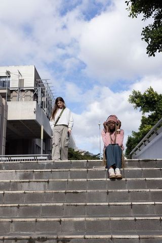 Young women relaxing on urban campus stairs listening to music and using smartphone