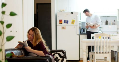Woman reading on sofa with man in kitchen background