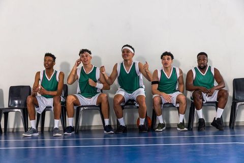 Diverse teammates cheering from sidelines on basketball court