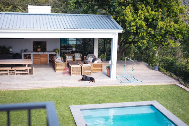 This image showcases a modern house exterior featuring a swimming pool and a well-maintained garden. The patio is furnished with comfortable outdoor furniture, creating a relaxing atmosphere. Ideal for use in real estate listings, home design inspiration, and lifestyle blogs focusing on outdoor living and home improvement.