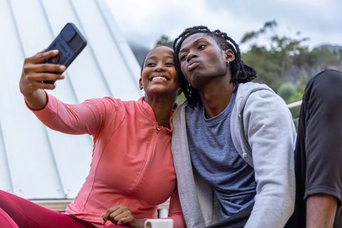 African american couple taking selfie on rooftop terrace after exercise, urban lifestyle