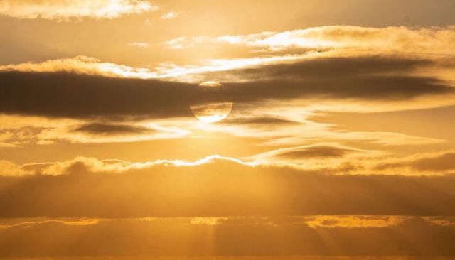 Sun disk breaking through layered clouds casting golden beams over horizon at twilight