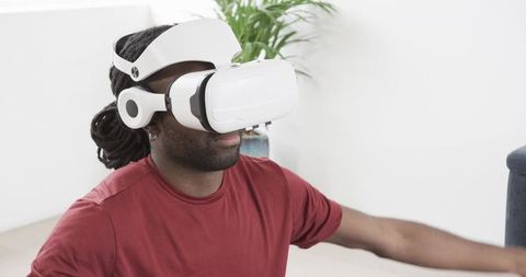 African American man experiencing virtual reality home wearing white VR headset reaching