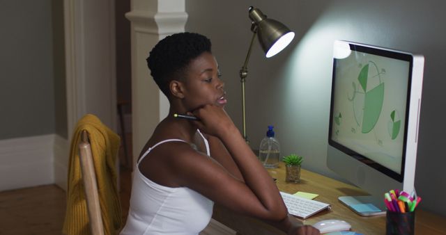 Young woman intently analyzing data on a computer screen in a home office. Ideal for depicting remote work, data analytics, business operations, and concentration in modern home settings. Can be used for articles related to telecommuting, home office setups, and professional women in tech.