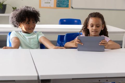 Multicultural students using tablet in classroom, sharing digital learning and teamwork