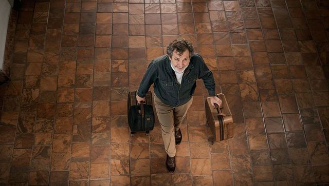 Walking traveler carrying two suitcases across terracotta tiled hall overhead perspective