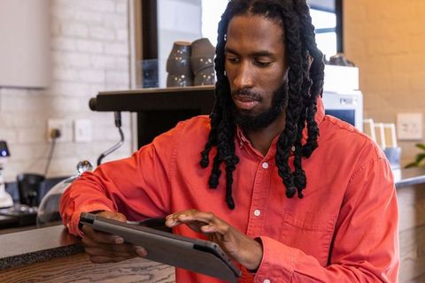 African american man using tablet at cafe counter wearing red shirt and dreadlocks