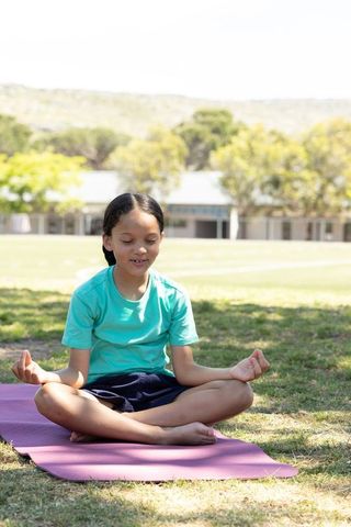 Asian child meditating on purple mat on school lawn practicing mindfulness and yoga