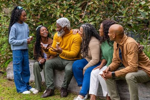 Multigenerational african american family sharing flower on garden log showing warm autumn bond