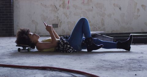 Young Woman Relaxing on Skateboard with Smartphone in Urban Space