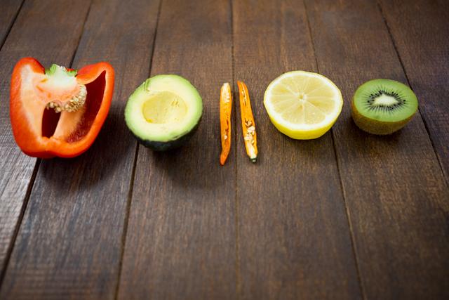 Assorted fresh vegetables and fruits including bell pepper, avocado, chili, lemon, and kiwi arranged on a wooden surface. Ideal for use in health and wellness blogs, nutrition articles, recipe websites, and food-related marketing materials.