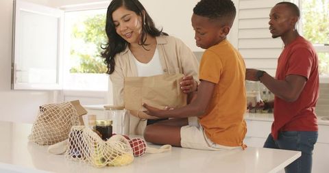 Diverse family unpacking groceries in sunlit modern kitchen, preparing healthy meal together