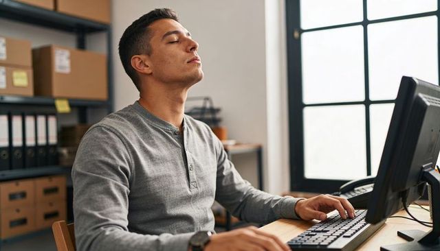 Young man pausing at workstation, taking deep breath and stretching neck