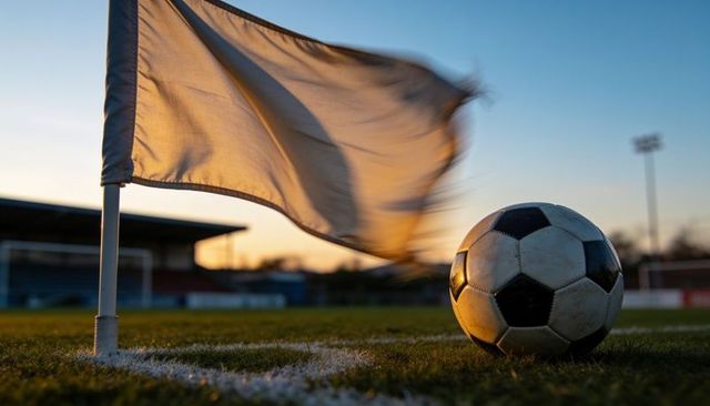 Glowing scuffed black and white soccer ball on corner arc with billowing flag at sunset