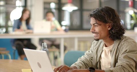 Smiling African American coworker working on laptop in modern casual coworking space with plants