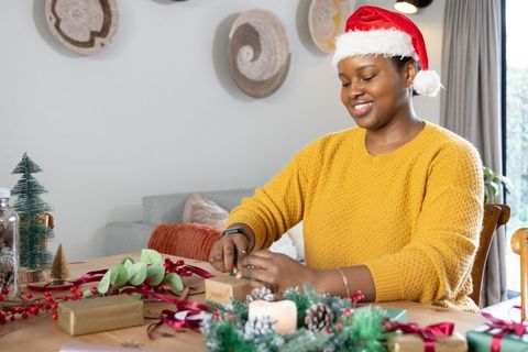 African american woman wearing santa hat wrapping christmas gifts at cozy dining table