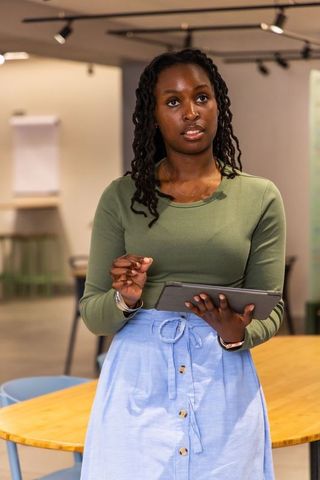 African american woman presenting with tablet in modern coworking space, professional speaker
