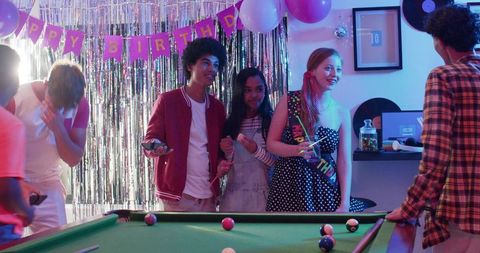 Young Friends Celebrating Birthday Around Pool Table with Neon Balloons and Fringe